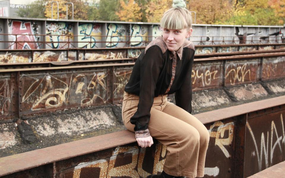 Porträt von Marie Pooth, sie sitzt auf einer alten Bahnbrücke, im Hintergrund sind Graffitis